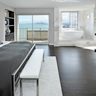 Modelo de dormitorio principal, minimalista, grande, sin chimenea, con paredes blancas, suelo de madera oscura, marco de chimenea de baldosas y/o azulejos y suelo marrón