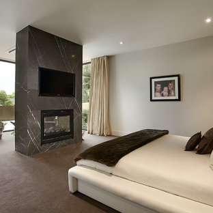 Large contemporary bedroom in Melbourne with white walls, carpet, a stone fireplace surround and a two-sided fireplace.