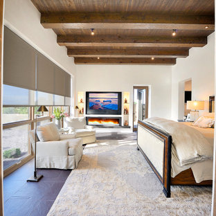 Modelo de dormitorio principal, de estilo americano, grande, con paredes blancas, suelo de pizarra, chimenea lineal, marco de chimenea de yeso y suelo marrón