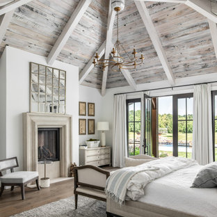Foto de dormitorio principal, clásico renovado, grande, con paredes blancas, suelo de madera en tonos medios, chimenea tradicional y marco de chimenea de piedra