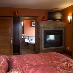 Ejemplo de dormitorio principal, de estilo americano, grande, con parades naranjas, suelo de madera clara, chimenea de doble cara y marco de chimenea de baldosas y/o azulejos