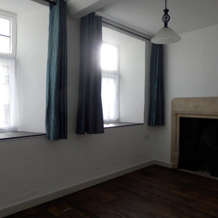 Modelo de habitación de invitados tradicional, de tamaño medio, con paredes blancas, suelo de madera oscura, estufa de leña, marco de chimenea de piedra y suelo marrón