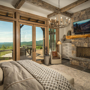 Imagen de habitación de invitados rústica con paredes blancas, chimenea tradicional, marco de chimenea de piedra y suelo marrón