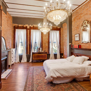 Modelo de dormitorio principal, bohemio, grande, con paredes grises, suelo de madera en tonos medios, chimenea tradicional y marco de chimenea de piedra