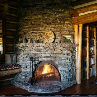 Modelo de dormitorio principal, rústico, grande, con suelo de madera en tonos medios, chimenea de esquina y marco de chimenea de piedra