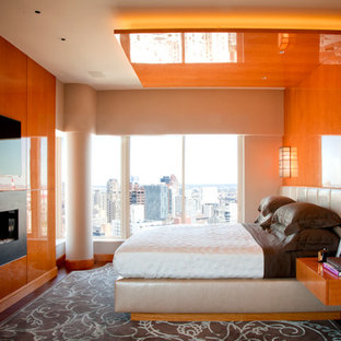 Imagen de dormitorio principal, contemporáneo, de tamaño medio, con parades naranjas, suelo de madera en tonos medios, chimenea lineal y marco de chimenea de metal