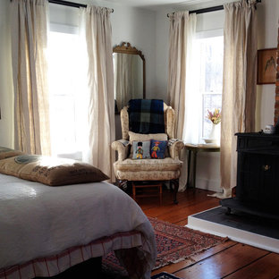 Foto de habitación de invitados campestre, de tamaño medio, con paredes blancas, suelo de madera en tonos medios, estufa de leña y marco de chimenea de ladrillo