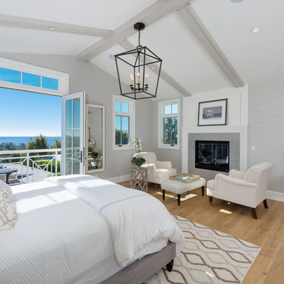 Large beach style master medium tone wood floor and brown floor bedroom photo in Los Angeles with gray walls, a standard fireplace and a tile fireplace