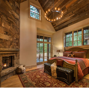 Imagen de dormitorio principal, rural, de tamaño medio, con suelo de madera clara, paredes beige, chimenea tradicional y marco de chimenea de piedra