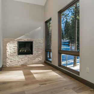 Immagine di una grande camera matrimoniale rustica con pareti grigie, parquet chiaro, camino sospeso, cornice del camino in pietra e pavimento marrone