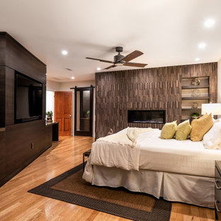 Immagine di una camera da letto minimal con pareti beige, pavimento in legno massello medio, camino lineare Ribbon, cornice del camino in legno, pavimento marrone e pareti in legno