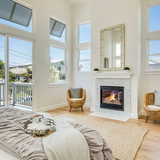 Design ideas for a mid-sized beach style master bedroom in Los Angeles with white walls, light hardwood floors, a standard fireplace, a stone fireplace surround and beige floor.