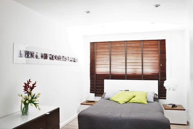 Imagen de dormitorio principal actual de tamaño medio con paredes blancas y suelo de contrachapado