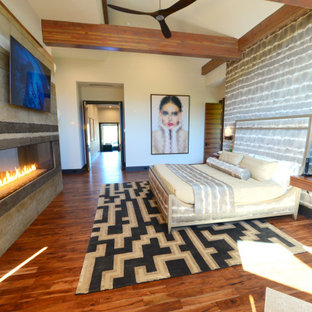 Modelo de dormitorio principal, moderno, grande, con paredes multicolor, suelo de madera en tonos medios, chimenea lineal, marco de chimenea de hormigón y suelo marrón
