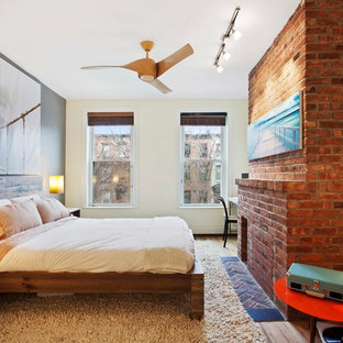 Inspiration pour une chambre parentale design de taille moyenne avec un mur beige, un sol en bois brun, un manteau de cheminée en brique, une cheminée standard et un sol beige.
