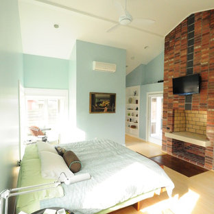 Réalisation d'une chambre parentale design de taille moyenne avec un mur bleu, un sol en bois clair, un manteau de cheminée en brique, une cheminée standard et un sol beige.