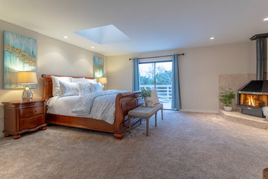 Foto de dormitorio principal costero de tamaño medio con paredes beige, moqueta, chimenea de esquina, marco de chimenea de metal y suelo beige