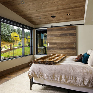 Modelo de dormitorio principal, rústico, de tamaño medio, con paredes blancas, suelo de madera en tonos medios y suelo marrón