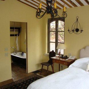Imagen de dormitorio principal, tradicional, de tamaño medio, sin chimenea, con paredes amarillas, suelo de piedra caliza y suelo marrón