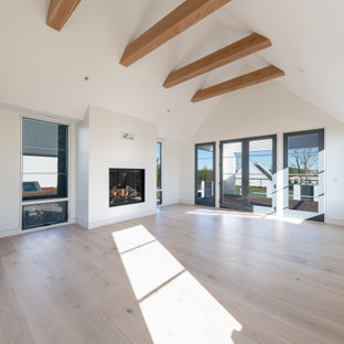 Esempio di una grande camera matrimoniale design con pareti bianche, parquet chiaro, camino sospeso, cornice del camino in intonaco e pavimento bianco