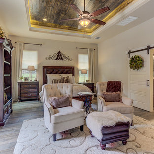 Imagen de dormitorio principal, rústico, de tamaño medio, con paredes beige, suelo de baldosas de porcelana, chimenea tradicional, marco de chimenea de piedra y suelo marrón