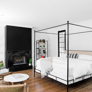 Ejemplo de dormitorio principal, tradicional renovado, de tamaño medio, con paredes blancas, suelo de madera en tonos medios, marco de chimenea de baldosas y/o azulejos, suelo marrón y chimenea lineal