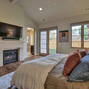 Imagen de dormitorio principal, rural, extra grande, con paredes beige, suelo de madera en tonos medios, chimenea tradicional y marco de chimenea de yeso
