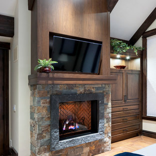 Diseño de dormitorio principal, rústico, con paredes beige, suelo de madera en tonos medios, chimenea tradicional, marco de chimenea de piedra y suelo negro