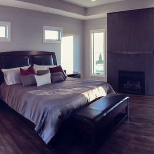 Imagen de dormitorio principal, actual, grande, con suelo de madera oscura, marco de chimenea de baldosas y/o azulejos, paredes beige y chimenea tradicional