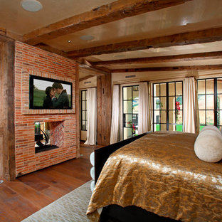 Diseño de dormitorio principal, mediterráneo, con paredes beige, suelo de madera oscura, chimenea de doble cara y marco de chimenea de ladrillo