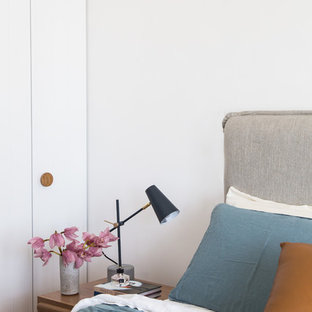 Modelo de dormitorio principal, contemporáneo, sin chimenea, con paredes blancas, suelo de madera clara, marco de chimenea de madera y suelo marrón