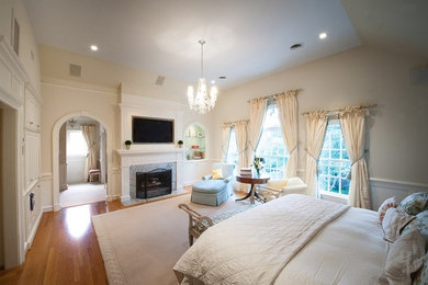 Example of a classic master light wood floor bedroom design in Richmond with beige walls, a standard fireplace and a wood fireplace surround