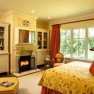 Imagen de dormitorio principal, de estilo americano, grande, con paredes beige, suelo de madera en tonos medios, chimenea tradicional y marco de chimenea de piedra