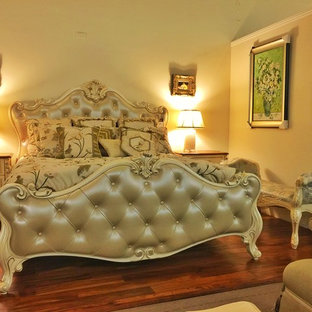 Modelo de dormitorio principal, tradicional, de tamaño medio, sin chimenea, con paredes beige, suelo de madera oscura y marco de chimenea de ladrillo