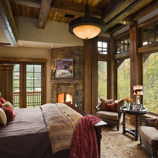 Foto de dormitorio rural con paredes beige, marco de chimenea de piedra y chimenea de esquina