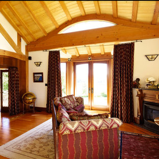 Modelo de dormitorio principal, grande, con paredes blancas, suelo de madera en tonos medios, chimenea de esquina y marco de chimenea de madera
