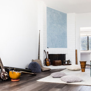 Diseño de dormitorio tipo loft, minimalista, grande, con paredes blancas, suelo de madera oscura, chimenea tradicional y marco de chimenea de ladrillo