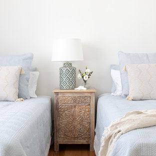 This is an example of a beach style bedroom in Other with white walls, medium hardwood floors and brown floor.