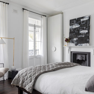 Photo of a contemporary master bedroom in Sydney with white walls, dark hardwood floors, a standard fireplace and brown floor.