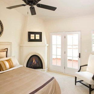 Modelo de dormitorio principal, mediterráneo, de tamaño medio, con paredes blancas, chimenea de esquina, moqueta, marco de chimenea de yeso y suelo beige