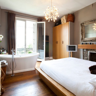 Foto de dormitorio principal, minimalista, de tamaño medio, con paredes grises, suelo de madera en tonos medios, chimenea tradicional y marco de chimenea de ladrillo