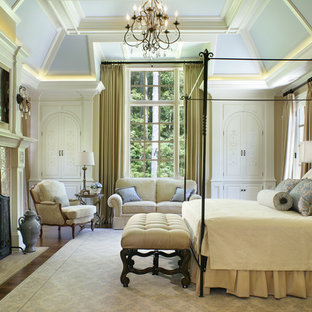 Exemple d'une grand chambre parentale chic avec un mur beige, un sol en bois foncé, une cheminée standard, un manteau de cheminée en plâtre et un sol marron.