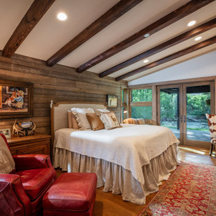 Rustikales Schlafzimmer mit weißer Wandfarbe, braunem Holzboden, Kamin, Kaminumrandung aus gestapelten Steinen, braunem Boden, freigelegten Dachbalken, gewölbter Decke und Holzwänden in Denver