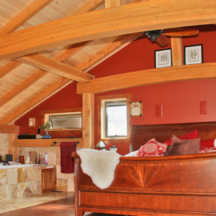 Modelo de dormitorio de estilo americano con paredes rojas, suelo de madera oscura, marco de chimenea de piedra y chimenea de doble cara
