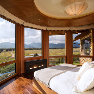 Modelo de dormitorio principal, contemporáneo, con suelo de madera en tonos medios y chimenea lineal
