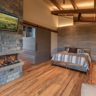 Diseño de dormitorio principal, actual, de tamaño medio, sin chimenea, con paredes marrones, suelo de madera clara, marco de chimenea de piedra y suelo marrón