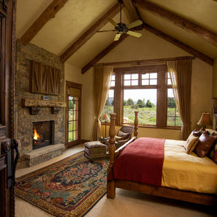 Foto de dormitorio principal, rural, grande, con paredes beige, moqueta, chimenea tradicional, marco de chimenea de piedra y suelo beige