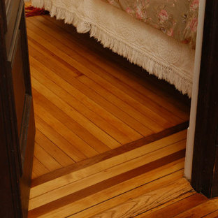 Modelo de dormitorio principal, clásico, de tamaño medio, con paredes blancas, suelo de madera clara, chimenea tradicional y marco de chimenea de ladrillo
