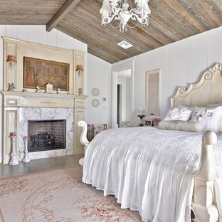 Foto de dormitorio romántico con paredes blancas, suelo de cemento, chimenea tradicional y marco de chimenea de piedra