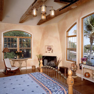 Foto de dormitorio principal, mediterráneo, de tamaño medio, con paredes beige, suelo de madera en tonos medios, estufa de leña, marco de chimenea de yeso y suelo marrón